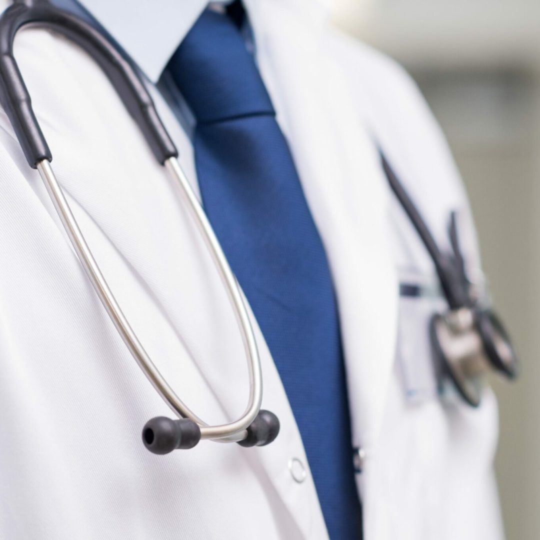 Detail of a stethoscope on the neck of a doctor with tie. Close up of a doctor with white lab coat stethoscope at hospital. Medical male doctor with lab coat and stethoscope at clinic.